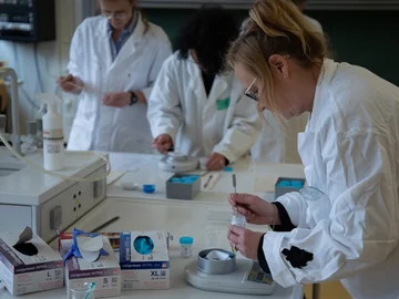 Drei Frauen in Laborkitteln wiegen chemische Stoffe mit Waagen ab.