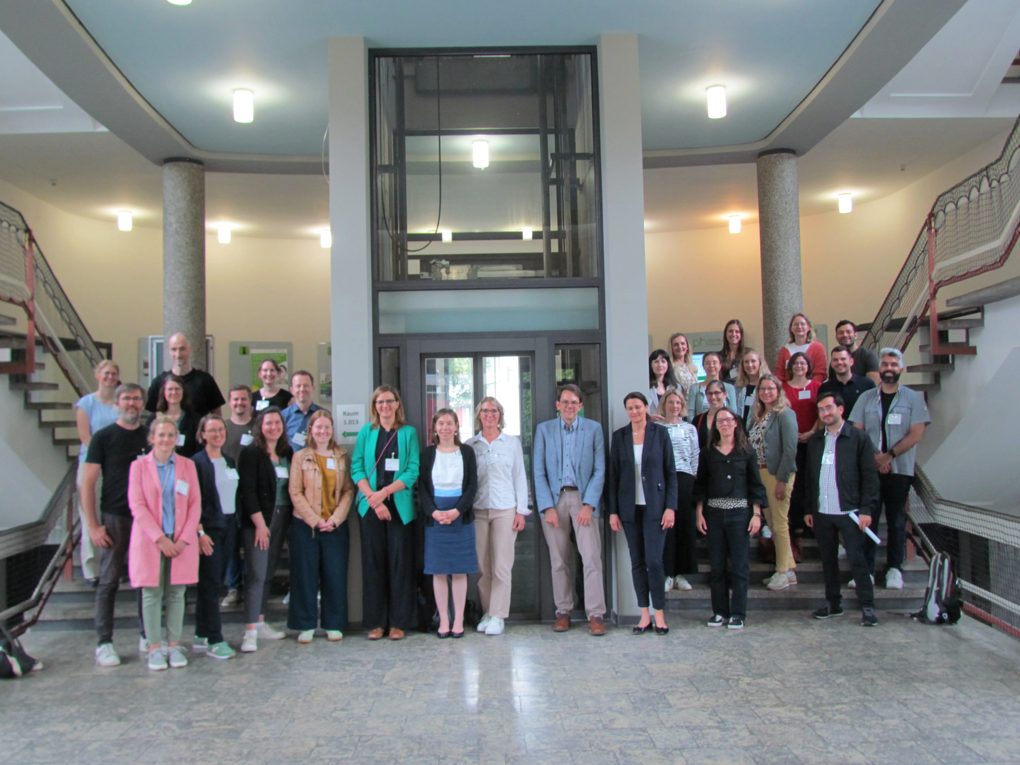 Eine Gruppe Wissenschaftlerinnen und Wissenschaftler steht in einem Foyer für die Gruppenaufnahme, viele mit Namensschildern.