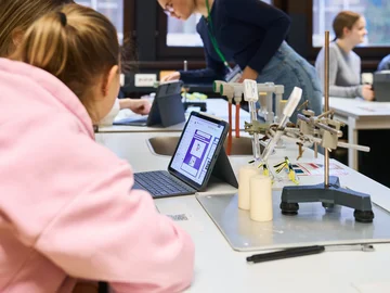 Schülerinnen sitzen in einem Physiklabor und schauen in Zweiergruppen auf Tablet-Bildschirme.