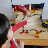 Ein Kind zeigt auf einen Spiegel auf einem Tisch, vor dem Spiegel liegen Bauklötze und Steinchen.