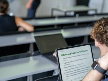 Ein junger Mann sitzt in einem Vorlesungsraum vor einem Laptop