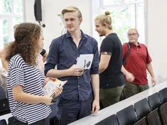 Zwei Studierende unterhalten sich, im Hintergrund stehen weitere Studierende.