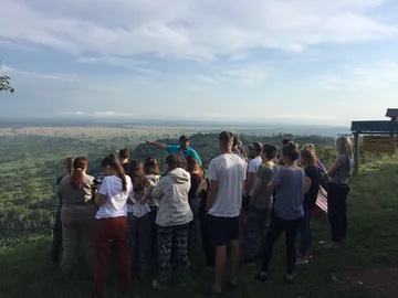 Das Bild zeigt die praktische Arbeit im Feld der Geographie. Zusehen ist eine Gruppe von Studierenden, die die umliegende Landschaft betrachten und einzelne Besonderheiten vom Dozenten im Feld durch Zeigen und Erklärungen erläutert bekommen.