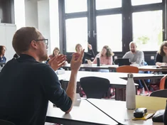Szene aus einer Weiterbildungsveranstaltung: Personen sitzen in einer Runde und diskutieren, ein Mann im Vordergrund spricht gerade
