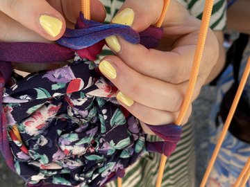 Hände mit gelben fingernägeln knüpfen bunten Stoff an Seile