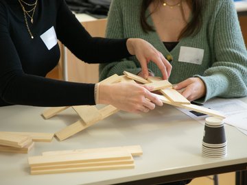 Zwei Frauen basteln eine Brücke aus Holzstückchen.
