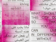 Typografisches Kunstwerk an einer Betonwand, bestehend aus mehrsprachigen Texttafeln in Rot-Weiß. Die Tafeln zeigen die Frage: „Was muss diese Stadt tun, damit du ohne Angst verschieden leben kannst?“ in mehreren Sprachen.