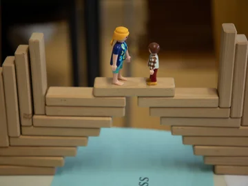 Zwei Legofiguren stehen auf einer Brücke aus Holzstückchen.