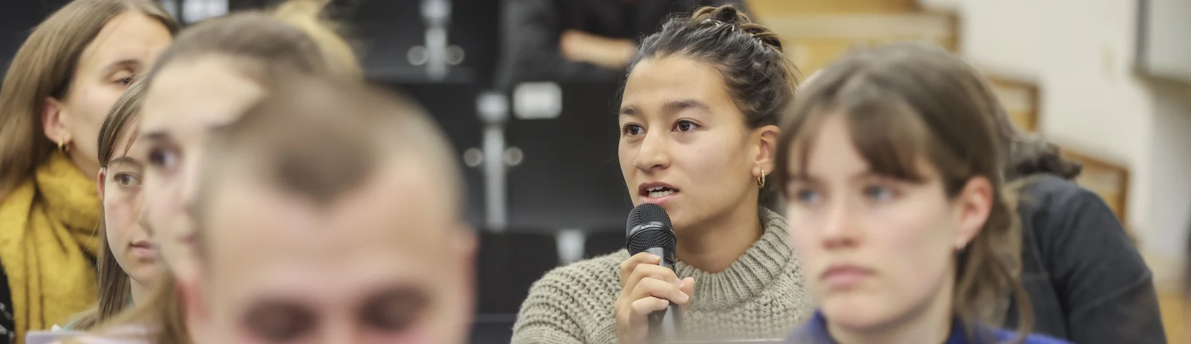 In einem Hörsaal spricht eine Studentin im Publikum in ein Mikrofon.