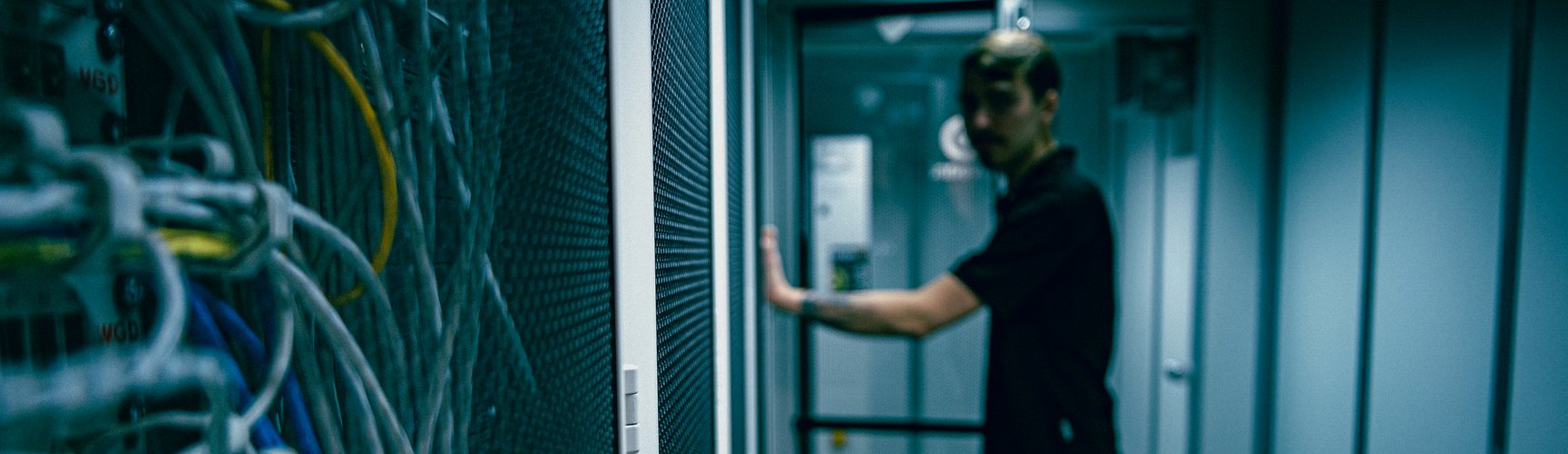 Ein Mann steht in einem Serverraum vor einem Schrank mit vielen Kabeln