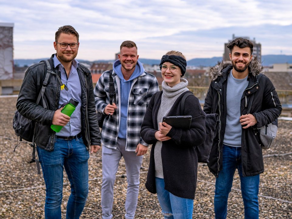 Vier Studierende stehen auf dem Dach der Hochschule und lachen in die Kamera