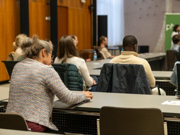 PHKA im Rathaus 2026: KI in der Bildung. Chancen gestalten – Qualität sichern. Publikum von hinten bei einem Vortrag. Eine Frau macht sich Notizen.