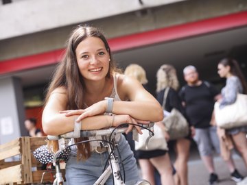 Eine Studentin lehnt auf dem Fahrradlenker auf dem Campus