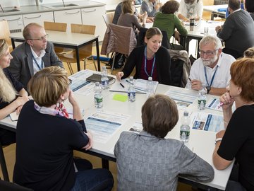 Tagungsteilnehmende sitzen gemeinsam an einem Tisch, auf dem Tisch liegen Plakate.