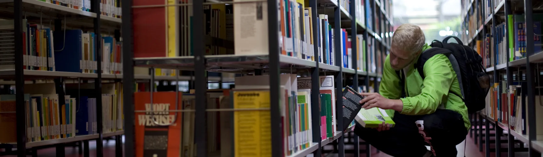 Ein Student sucht ein Buch in einem Bücherregal der Hochschulbibliothek
