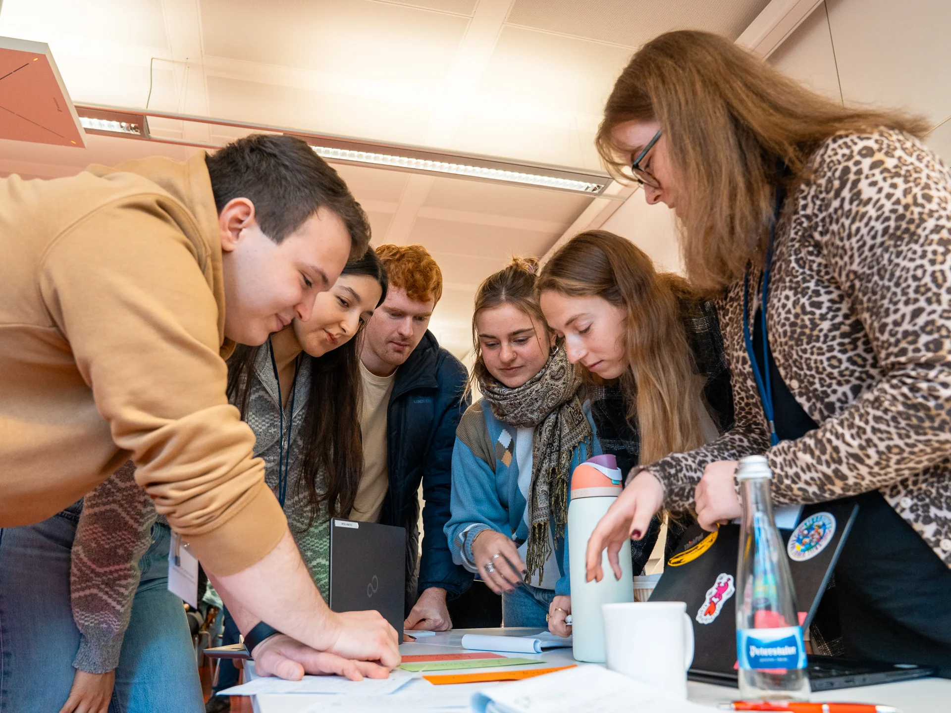 A group of students standing around a table exchanging ideas.