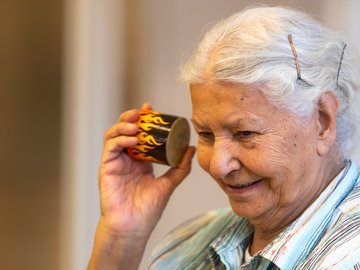 Seniorin hält eine kleine Trommel ans Ohr