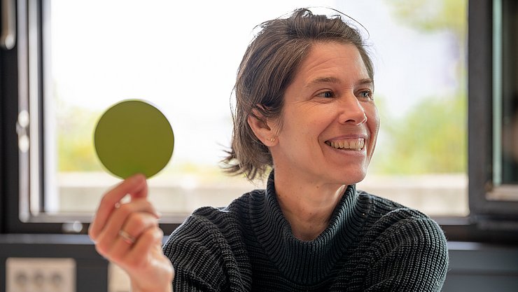 Key Visual MA Erwachsenenbildung Eine Person hält einen grünen Punkt aus Papier in die Höhe.