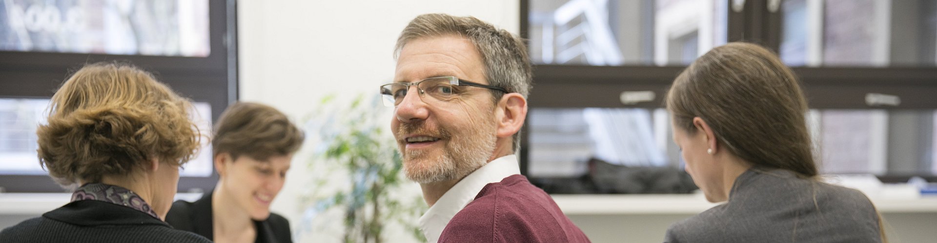 eine sitzende Gruppe von vier Personen. Eine dieser Personen dreht sich um und blickt in die Kamera.