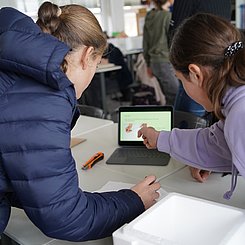 Zu sehen sind Schülerinnen, die mithilfe einer Anleitung eine Sonde bauen.