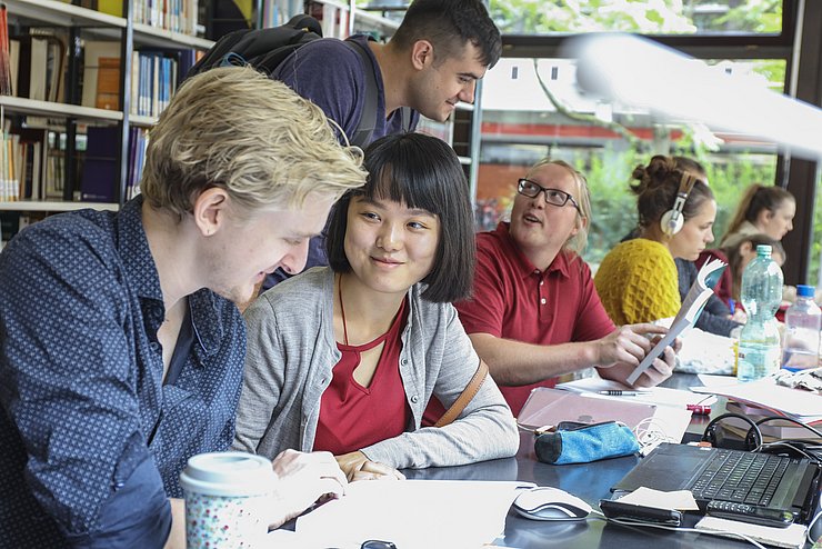 Die Lernstunde 023 Studierende lernen im ruhigen Bereich der Bibliothek der PH Karlsruhe. Hinter ihnen, sind Bücherregale zu sehen. Sie befinden sich im Gebäude 2.