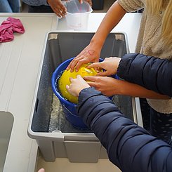 Zu sehen sind Schülerinnen, die mithilfe des archimedischen Prinzips das Volumen des Ballons bestimmen.