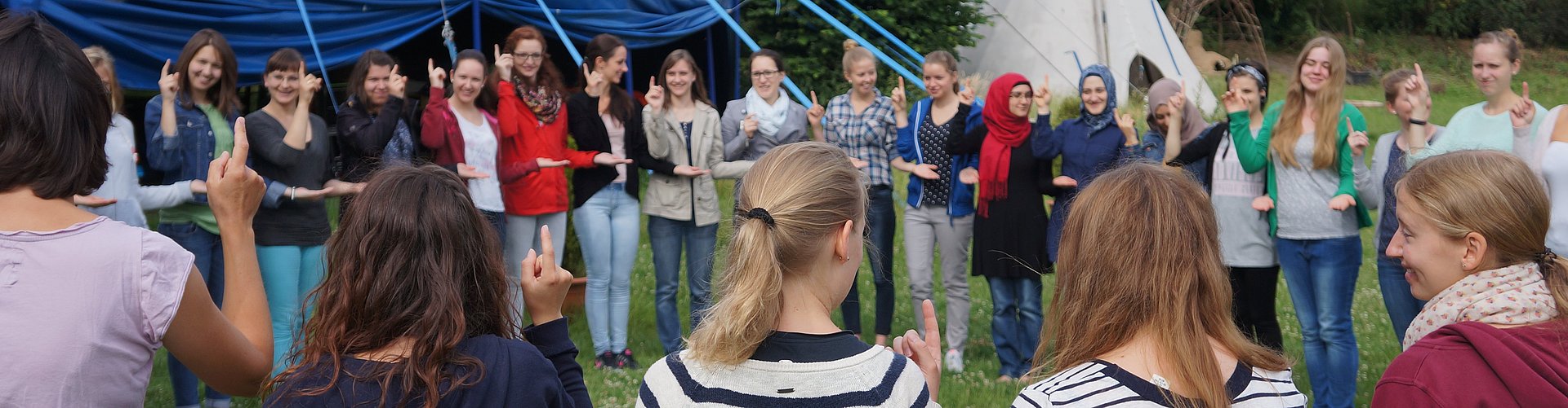 Menschen stehen auf einer Wiese vor einem bunten Zelt.